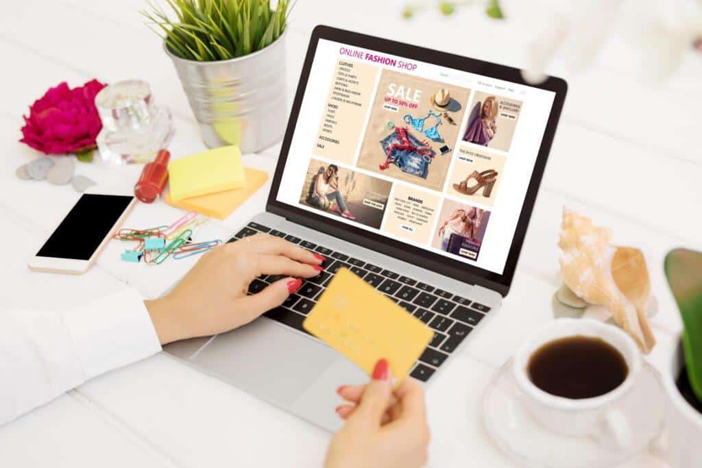 Persona realizando una compra online en una tienda de moda desde un portátil, con tarjeta de crédito en mano