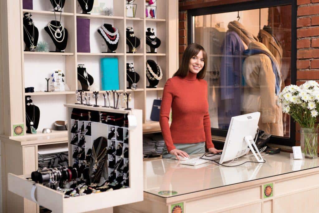 Dependienta atendiendo en una joyería, con expositores de collares y pulseras en el fondo